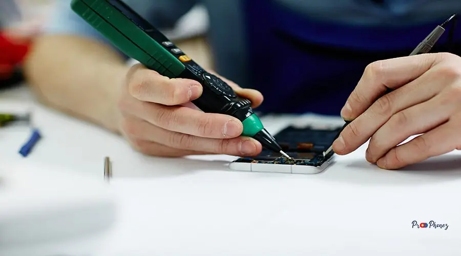 Checking Voltage in Mobile Device Closeup shot of male hands working on disassembling circuit board in mobile phone device and checking electric current with multimeter tool on table in maintenance shop with assorted tools
