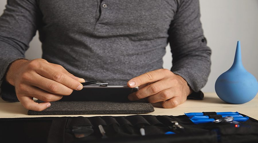 Close view, master uses pincher tool to remove sim card slot from smart phone while disassembling it