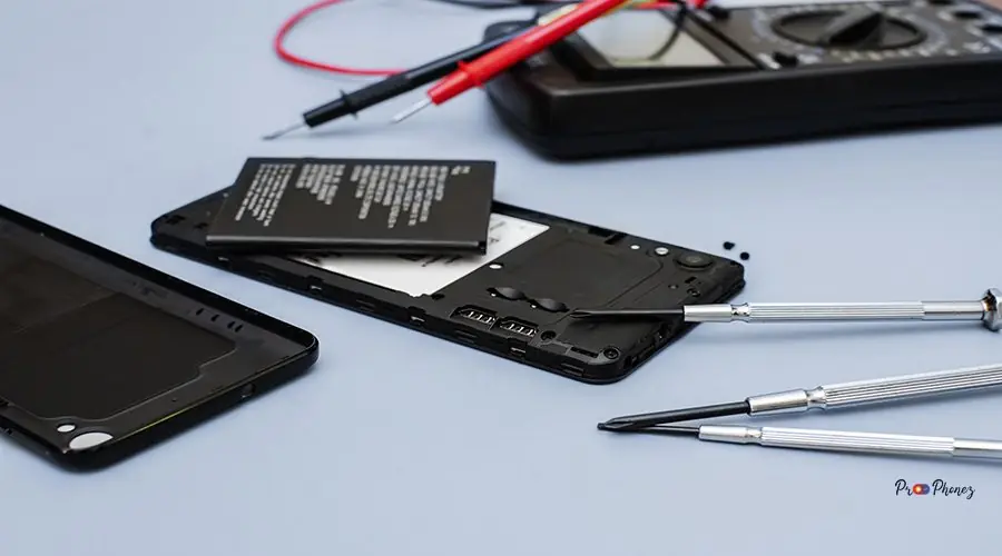 Disassembled mobile phone in the service centre Disassembled smartphone, battery replacement process. The back cover of the smartphone has been removed, revealing the battery and internal components. There are precision screwdrivers and multimeter probes lying around the phone.