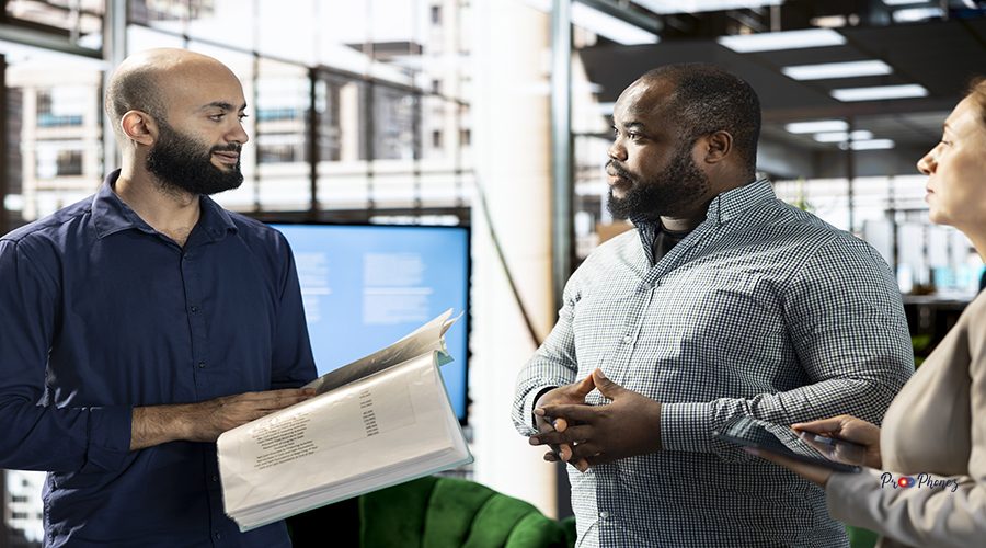 Middle Eastern businessman talking with coworker in startup company, looking at financial business documents. Diverse team of office clerks checking accounting figures in paperwork