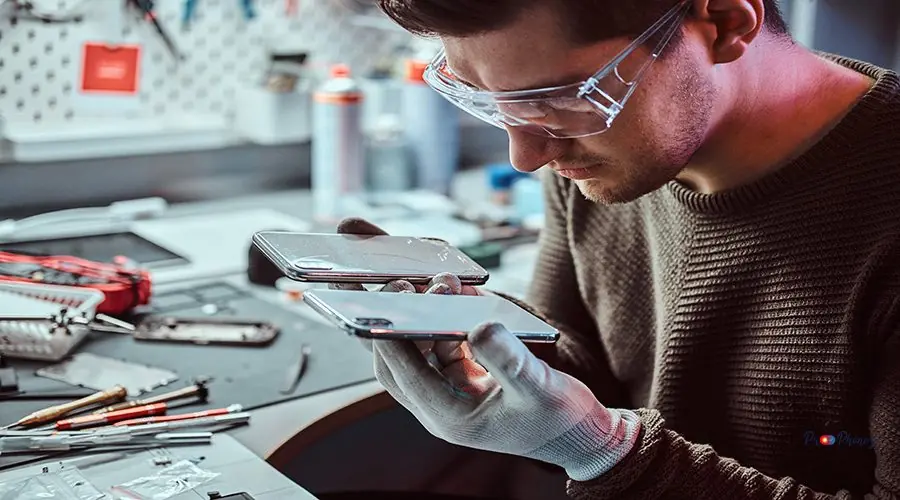 Technician holds two identical smartphones for comparison, in one hand broken and in another new Electronic technician holds two identical smartphones for comparison, in one hand broken and in another new