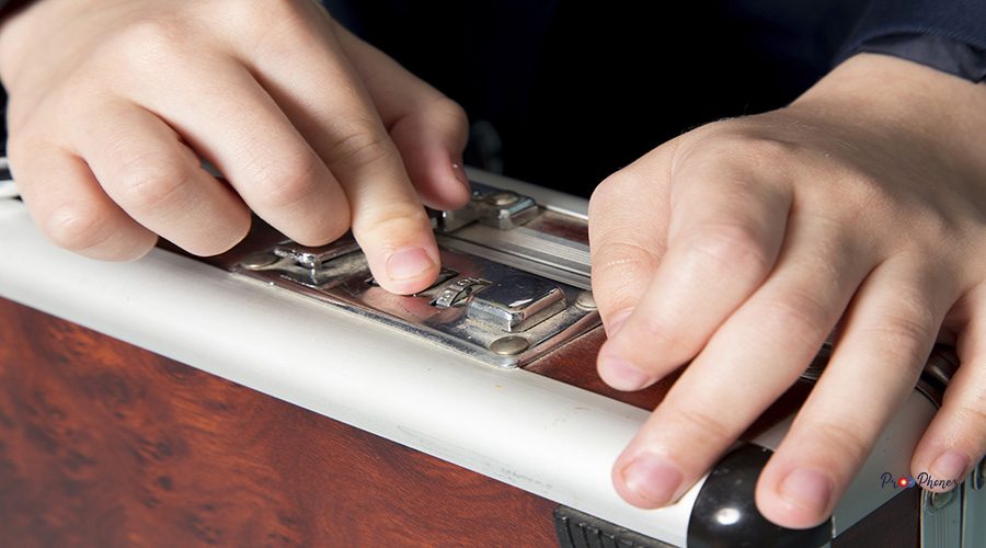 a front view cute business boy in blue classic suit posing holding brown-silver suitcase business work fashion on the blue background