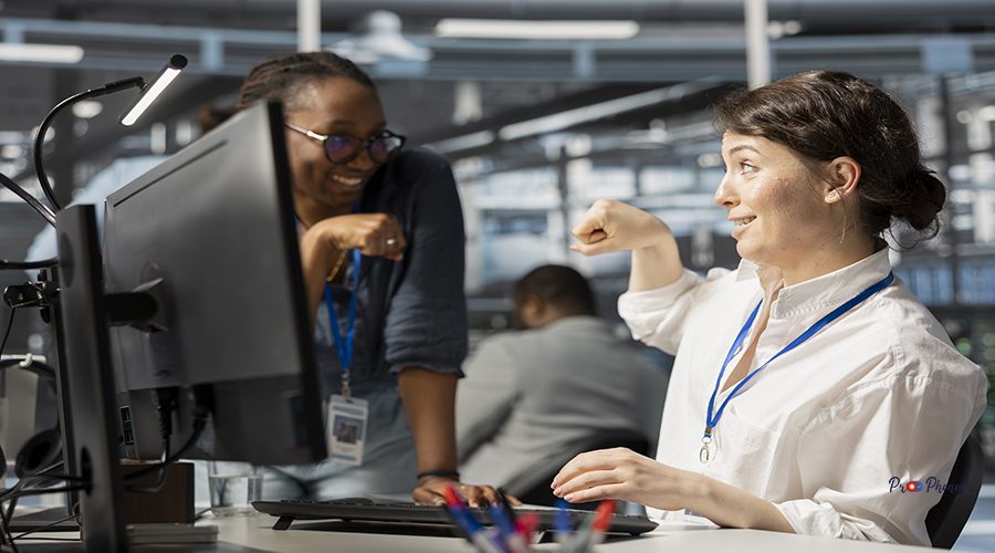 Happy server hub team leader does fist bump with worker after completing operations. Cheerful manager congratulating engineer in data center after checking report showing stable performance indicators