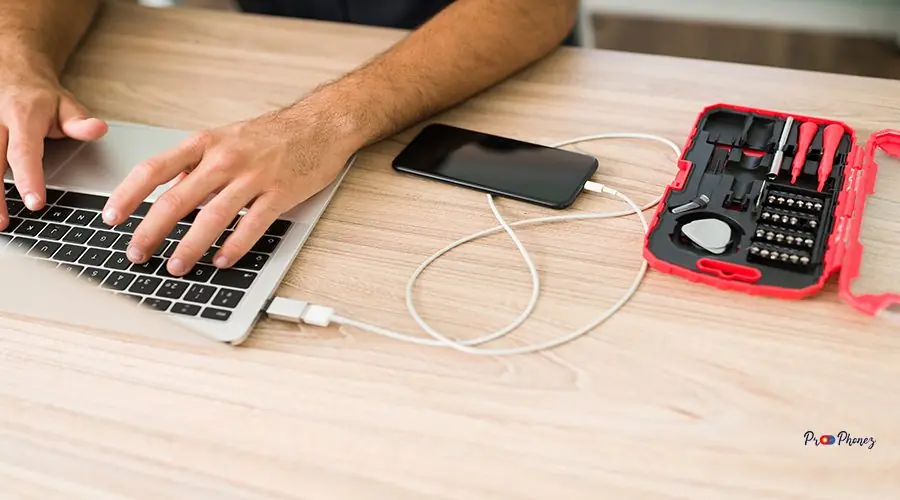 Doing a data backup before updating the software Hispanic male technician typing on laptop and connecting a smartphone to the computer to make a data backup at his repair shop