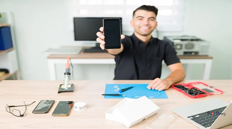 Cheerful technician holding a brand new phone Just as new. Happy young man showing a fixed smartphone. Smiling technician repairing the broken screen of a smartphone