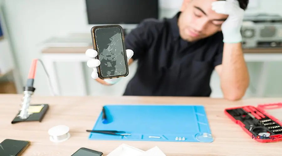 Stressed man repairing a broken old smartphone Look at this ugly smartphone. Upset male technician feeling worried while showing the cracked screen of a new smartphone