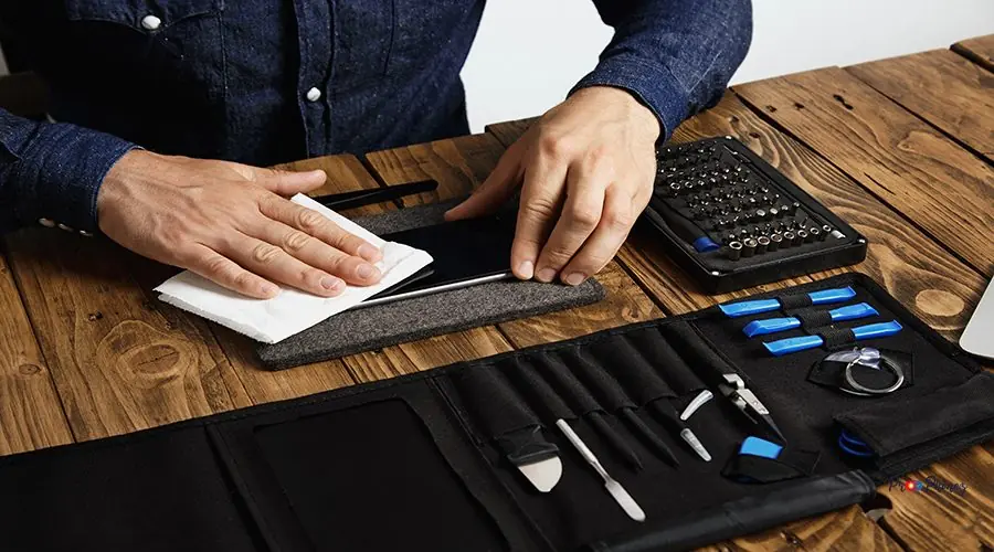Electronic repair service Master cleans mobile phone after successful restoration with white cloth near his professional instruments in tool bag on wooden table