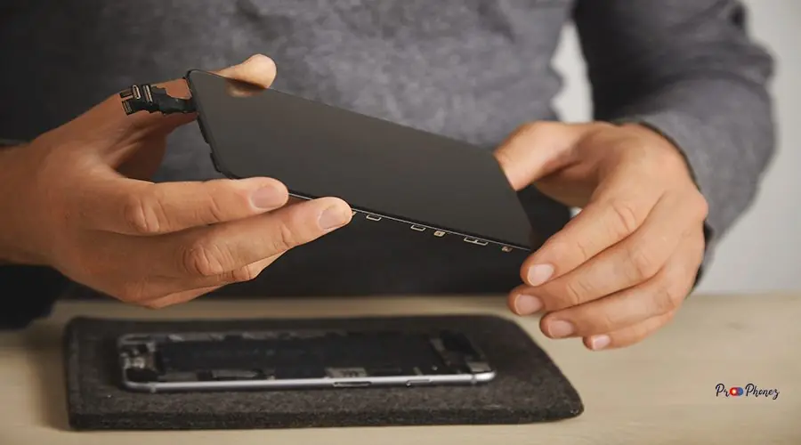 Computer and phone repairment service Master holds new screen for replacement above disassembled smartphone in his laboratory, close up