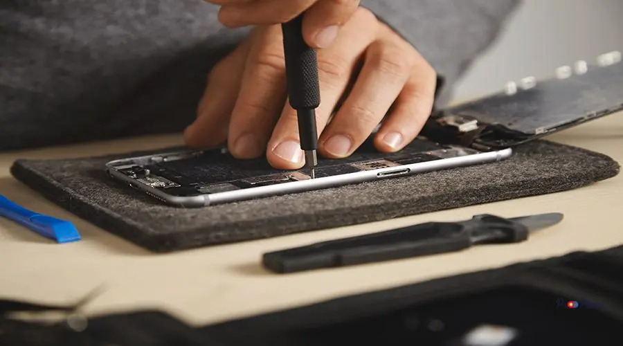Computer and phone repairment service Master uses driver to unscrew screws in smartphone electronic plates to fix it, closeup