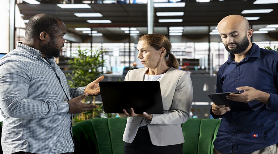 Multiracial workers using laptop device to write emails, solving tasks. Staff members typing on notebook keyboard in office, making sure documents are quality assurance compliant