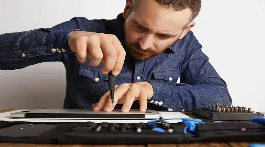 Electronic repair service Professional accurately unscrewing case of metallic slim laptop in his electric service lab near tool bag to clean and repair it, front view