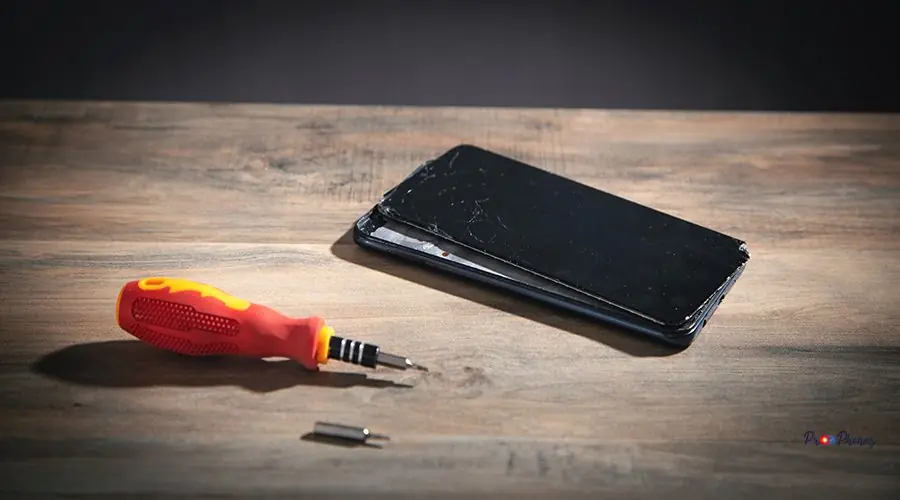 Screwdriver and broken smartphone on the wooden table. Repair se Screwdriver and broken smartphone on the wooden table. Repair service