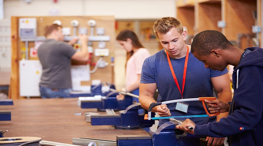 Teacher Helping Students Training To Be Electricians Using A Saw