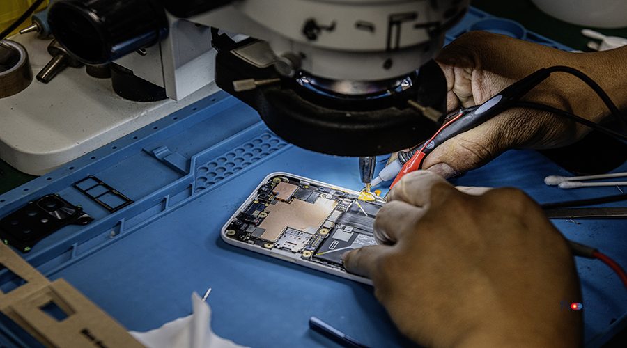 A technician repairing a mobile phone under a magnifying microscope on his blue work table against electromagnetic interference