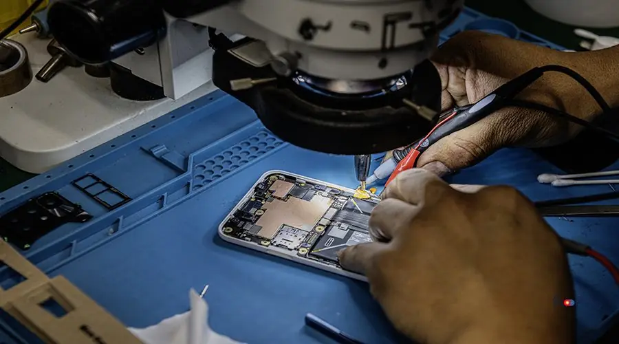 A technician repairing a mobile phone under a magnifying microsc A technician repairing a mobile phone under a magnifying microscope on his blue work table against electromagnetic interference