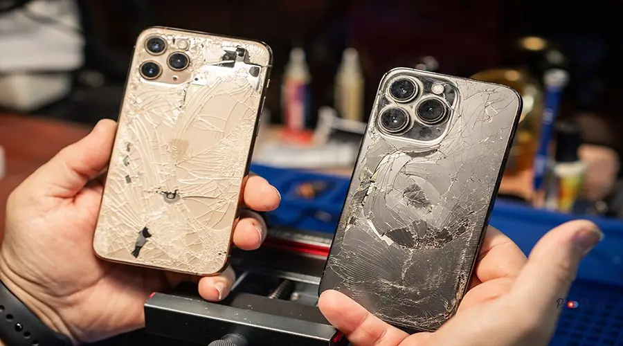 A technician repairs smartphones with broken glass at a phone repair service in the evening Technician focuses on repairing two smartphones with shattered screens in a busy service center.