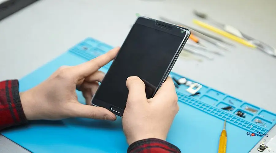 Unrecognizable male technician wearing plaid shirt sitting at hi Unrecognizable male technician wearing plaid shirt sitting at his workplace, turning on smart phone in his hands to find faults. Technology, modern electronics, repair and maintenance concept.
