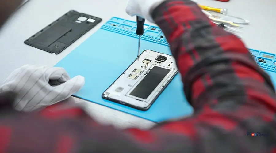 Back view of unrecognizable male technician wearing white antist Back view of unrecognizable male technician wearing white antistatic gloves and plaid shirt sitting at his desk and using precision screwdriver to remove screws on back of faulty mobile phone