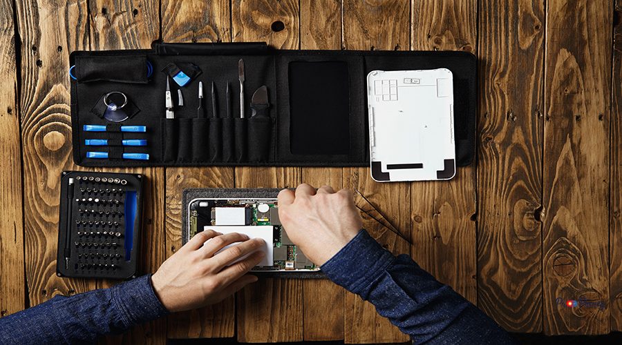 Top view master works on broken tablet to repair it near tool bag and on wooden table in service lab