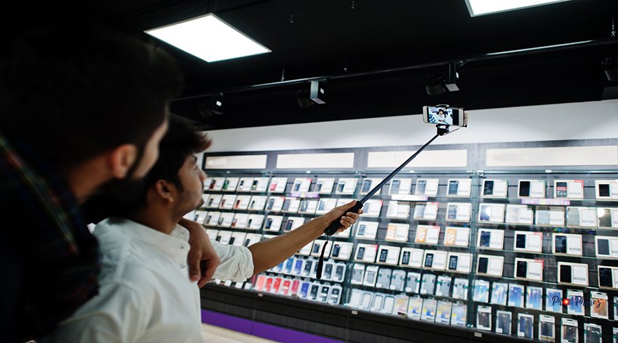Two indians mans customer buyer at mobile phone making selfie by monopod stick. South asian peoples and technologies concept. Cellphone shop.